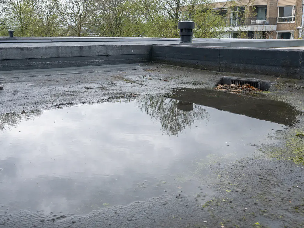 Plas water op een plat dak bij een deels verstopte afvoer