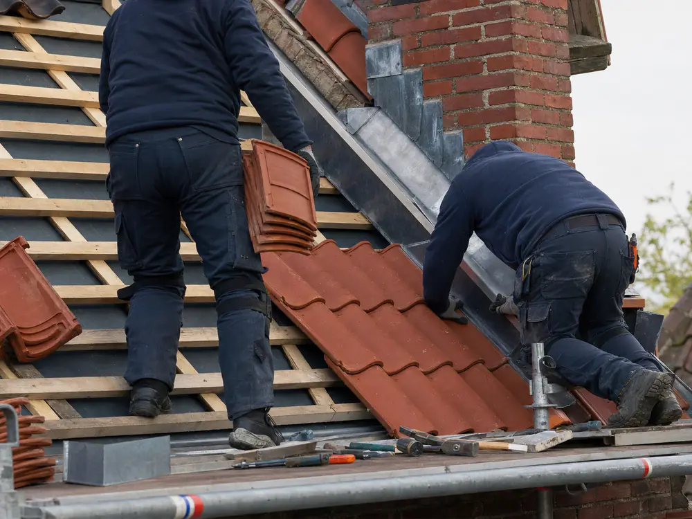 Twee dakdekkers aan het werk op een dak, in werkkleding