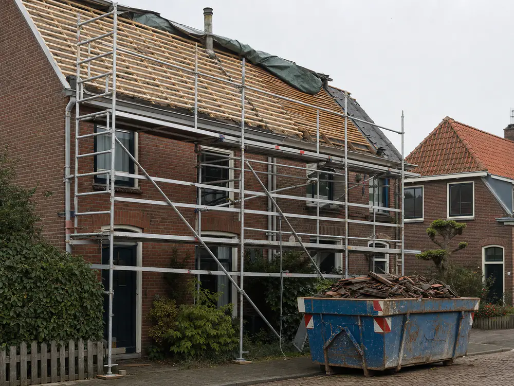 Steiger tegen een woning, met het dak deels open en de latten in het zicht